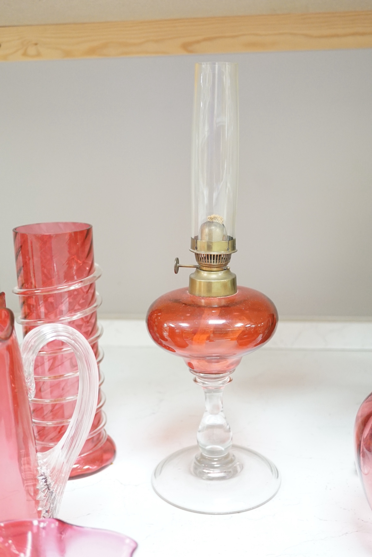 A quantity of cranberry glassware to include pair of vases with trailed decoration, jugs and an oil lamp, largest 38cm high. Condition - fair, some chipping